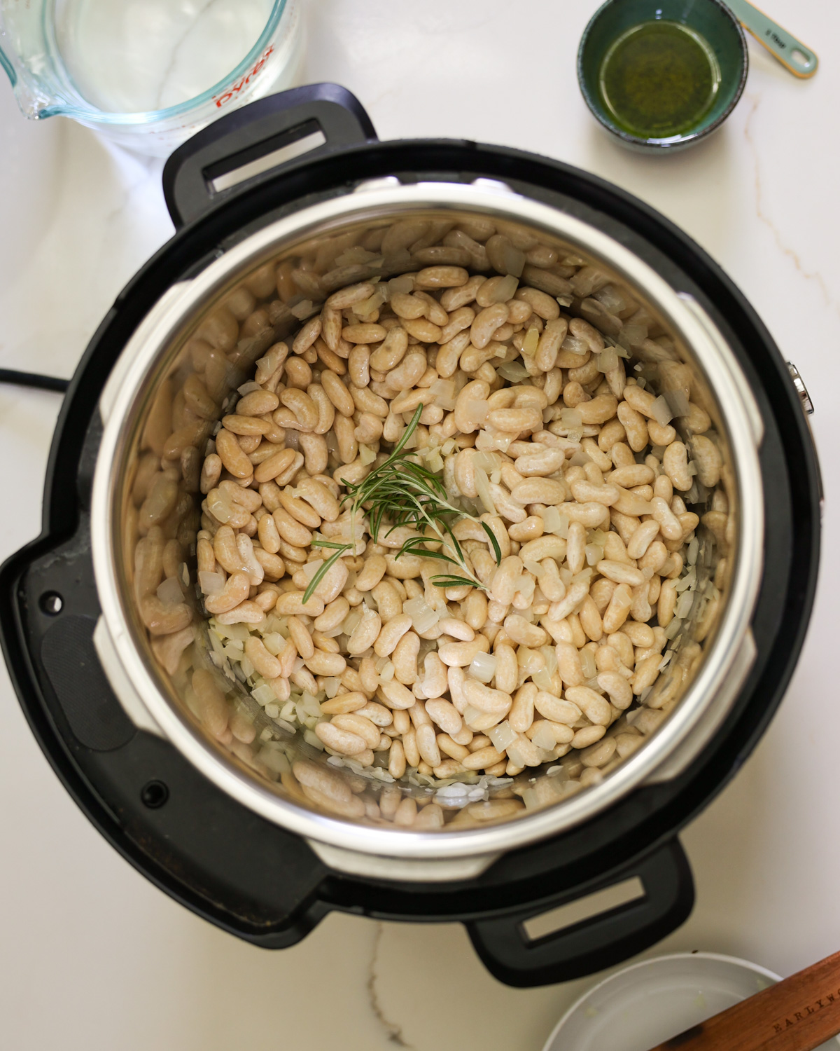 An Instant Pot with soaked white beans and rosemary.