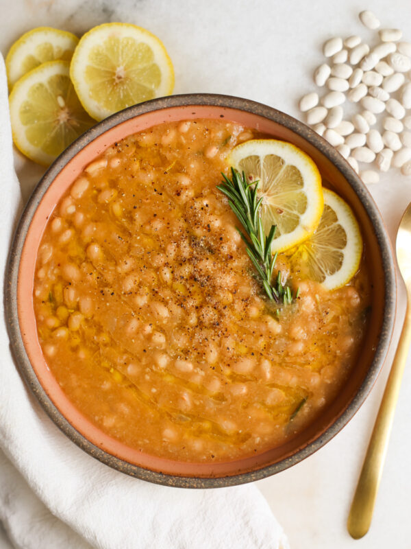 An overhead shot of a bowl of Instant Pot white beans with lemon and rosemary with a towel and spoon.