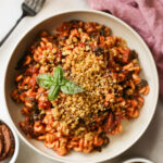 An overhead shot of a white bowl of Instant Pot Vegan Sausage Pasta with bread crumbs and a sprig of basil.