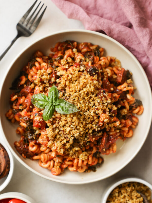 An overhead shot of a white bowl of Instant Pot Vegan Sausage Pasta with bread crumbs and a sprig of basil.