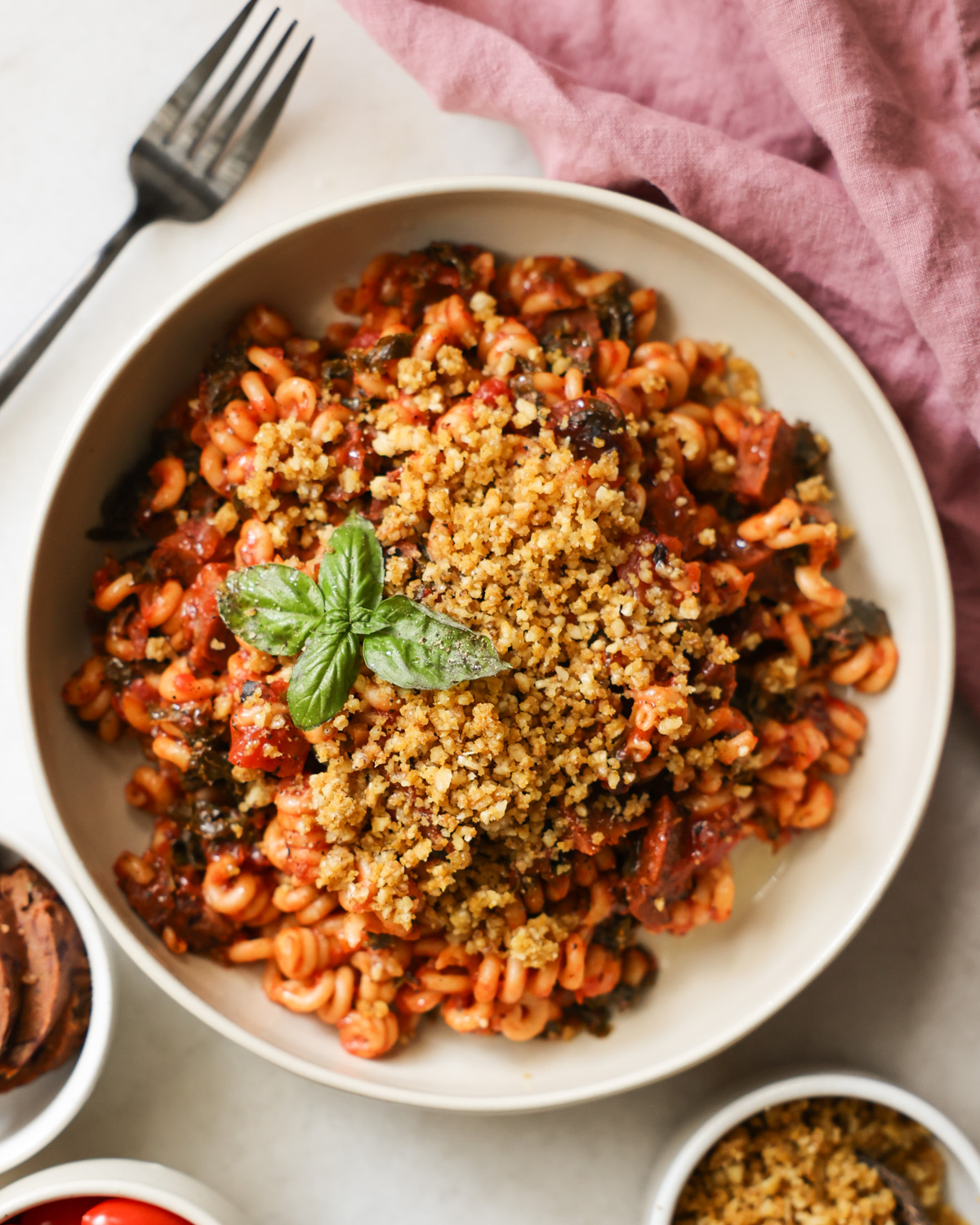 An overhead shot of a white bowl of Instant Pot Vegan Sausage Pasta with bread crumbs and a sprig of basil.