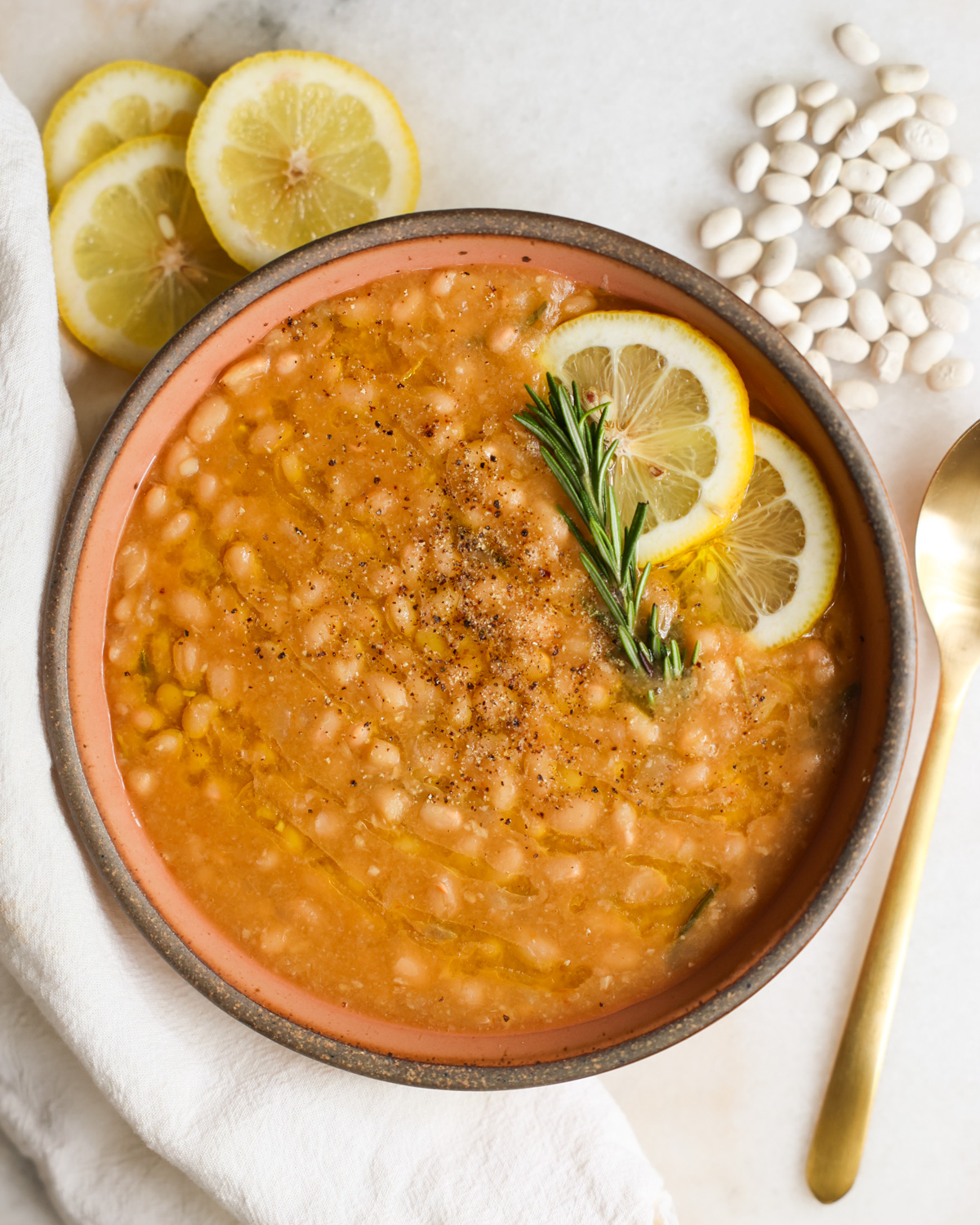 A bowl of Instant Pot white beans with lemon and rosemary garnish.