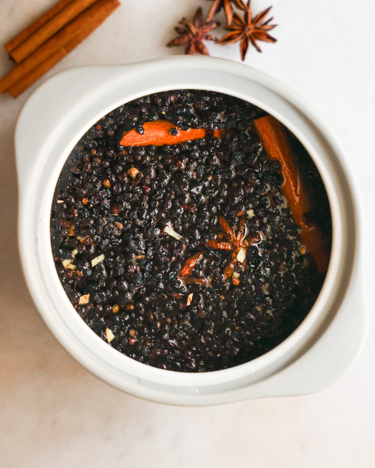 An overhead shot of a crock of elderberries simmered in water with spices.