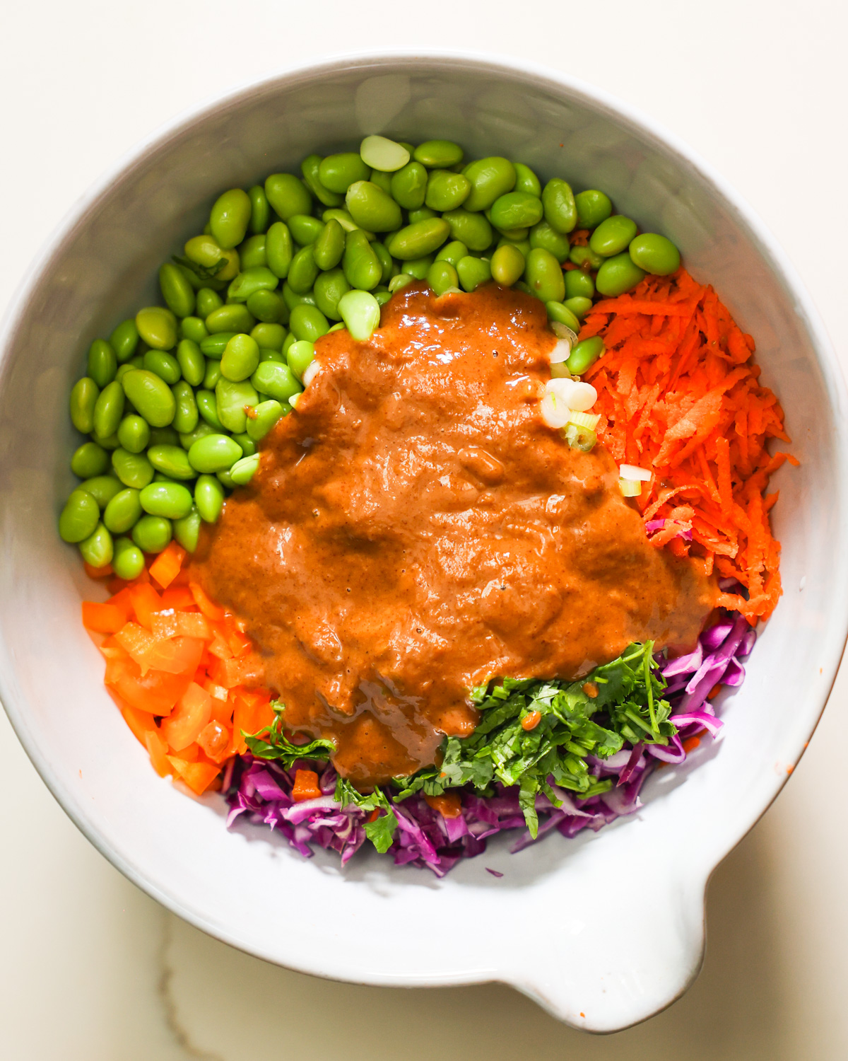 An overhead shot of a mixing bowl with the almond butter dressing poured over the edamame salad.