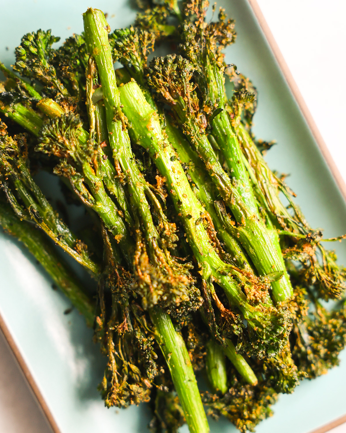 A close-up shot of the air fryer broccolini on a green plate.