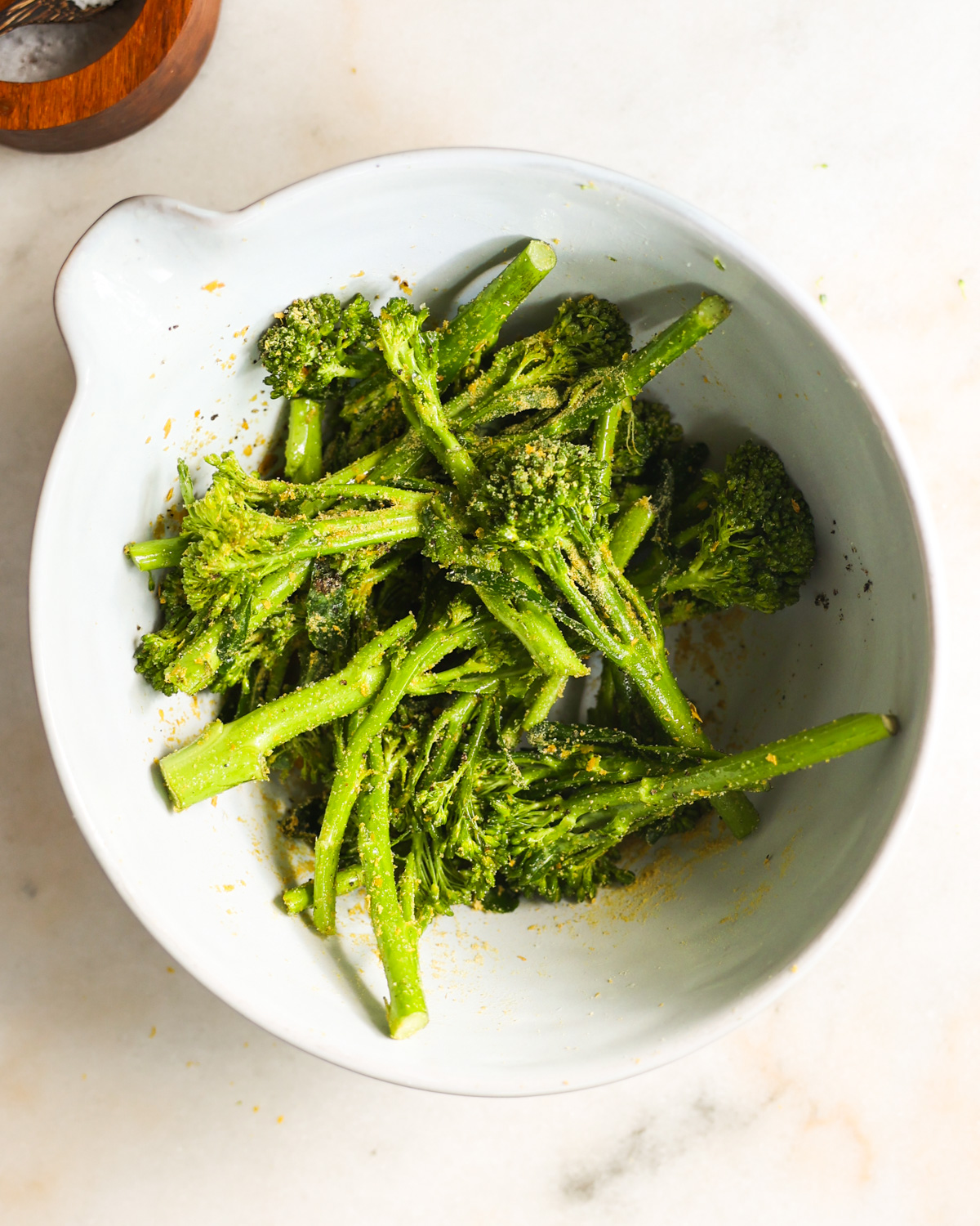 An overhead shot of the seasoned broccolini in a white mixing bowl.