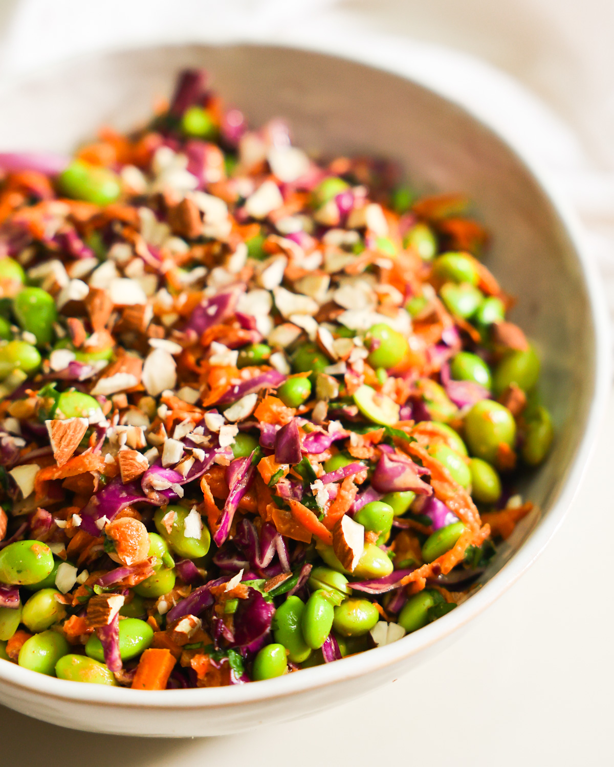 A close-up side shot of a bowl of edamame salad garnished with chopped almonds.