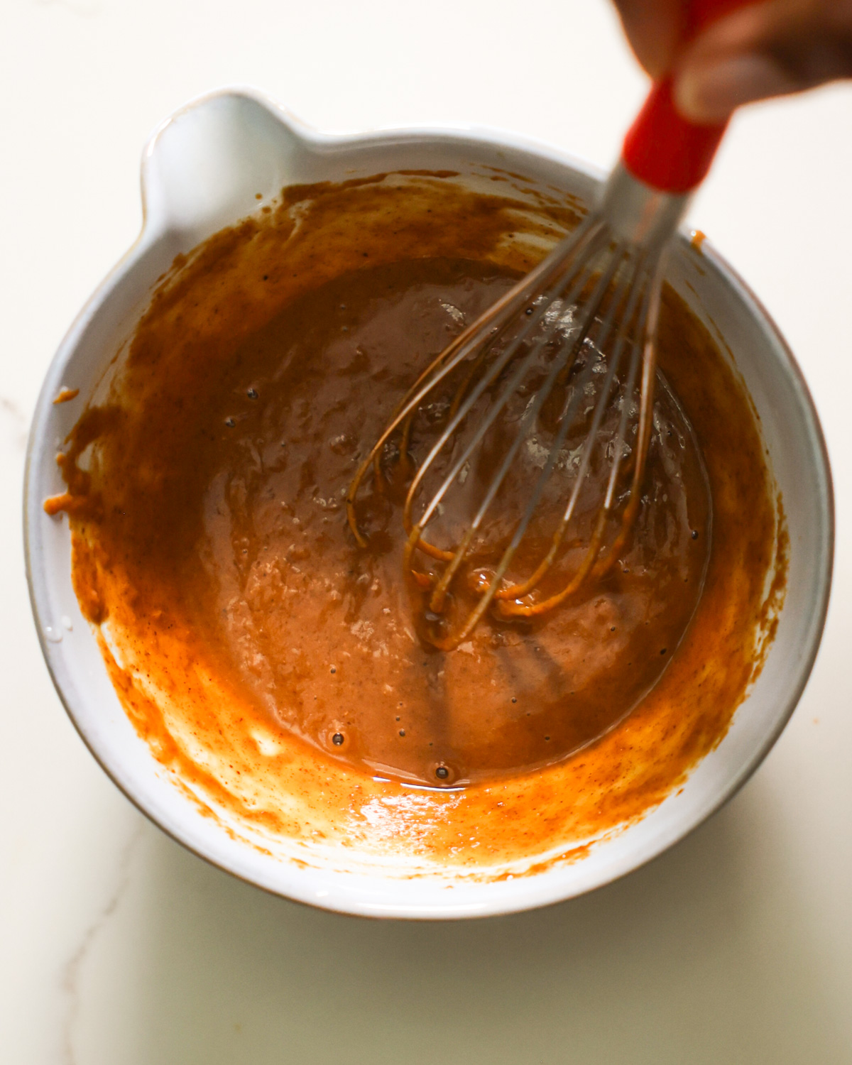 An overhead shot of a brown hand whisking a small bowl of almond lime dressing.