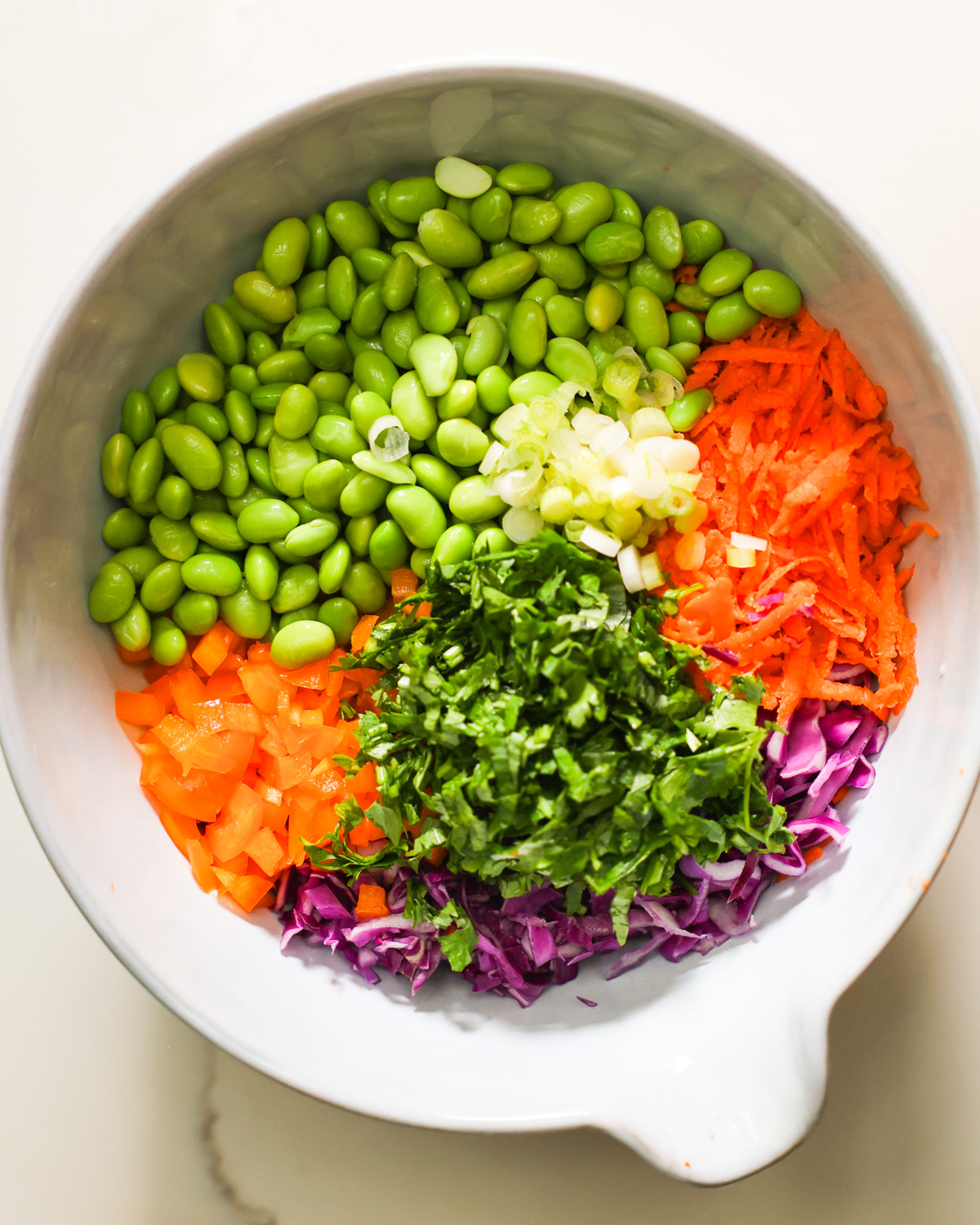 An overhead shot of a mixing bowl with the ingredients for edamame salad.