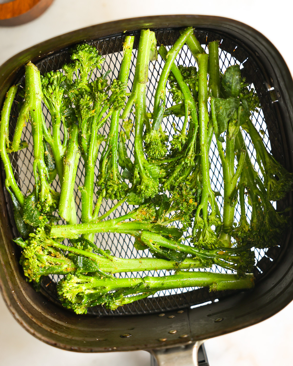 The seasoned broccolini in the air fryer basket.