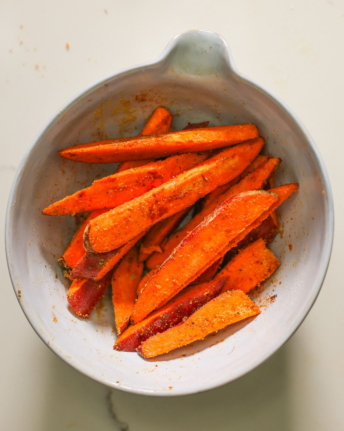 overhead of spiced sweet potato wedges in mixing bowl