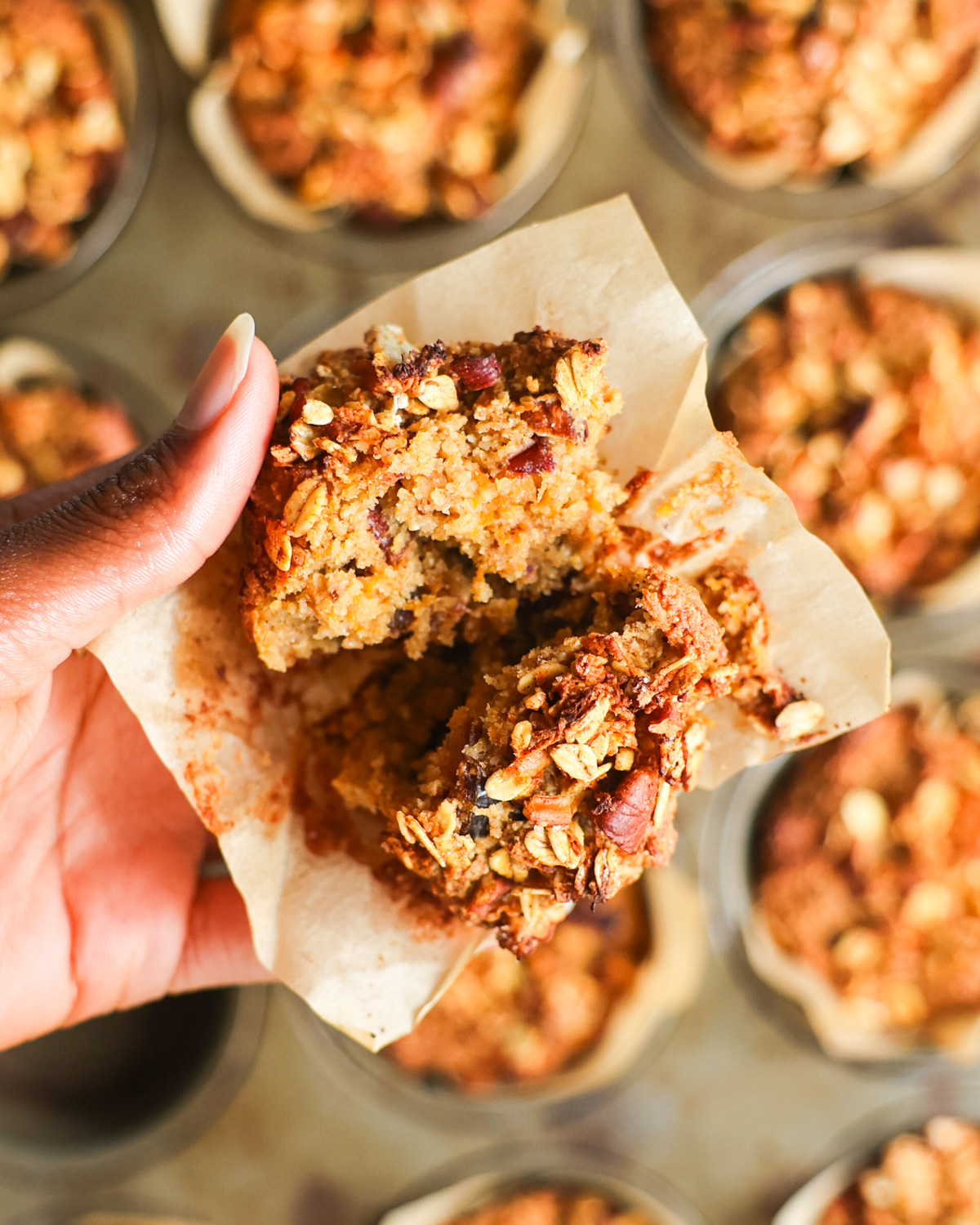 A close-up overhead shot of a brown hand holding an oat bran muffin split in half.