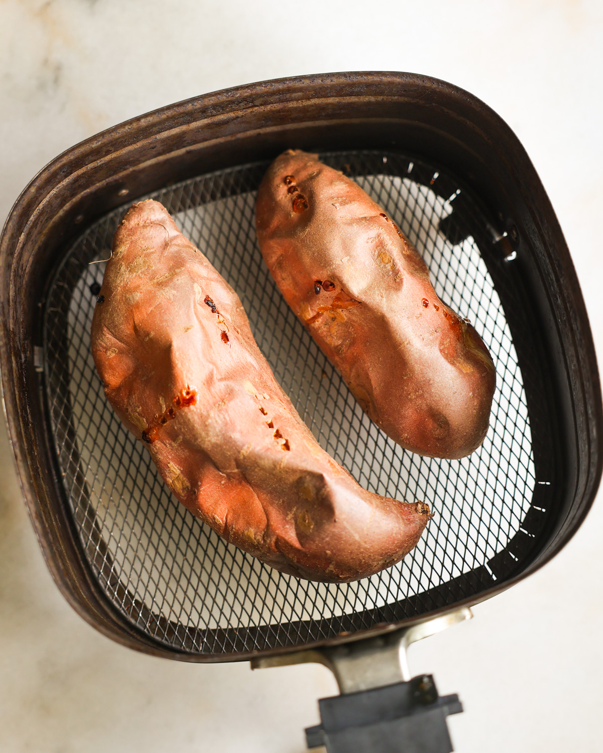 An overhead shot of two cooked air fryer sweet potatoes in the air fryer basket.