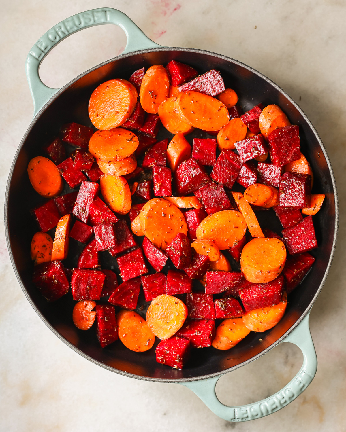 An overhead shot of the seasoned beets and carrots before roasting.