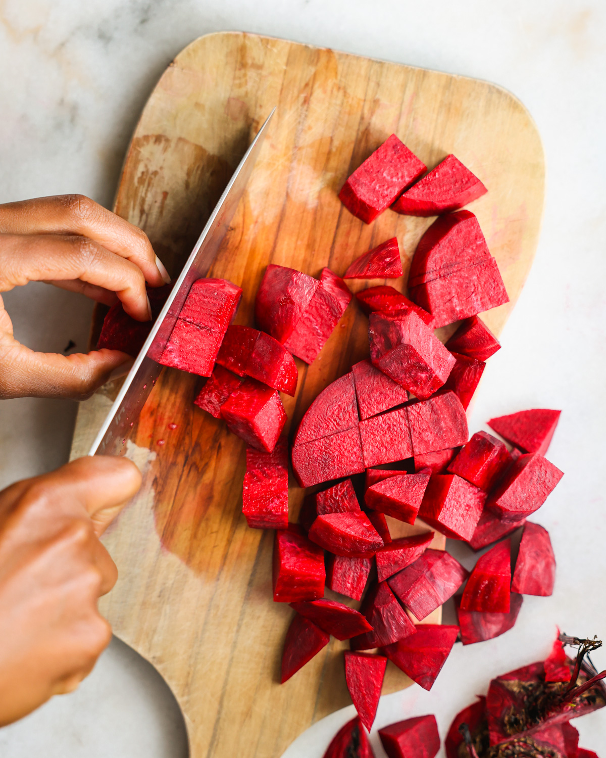 An overhead shot of brown hands slicing beets into chunks.