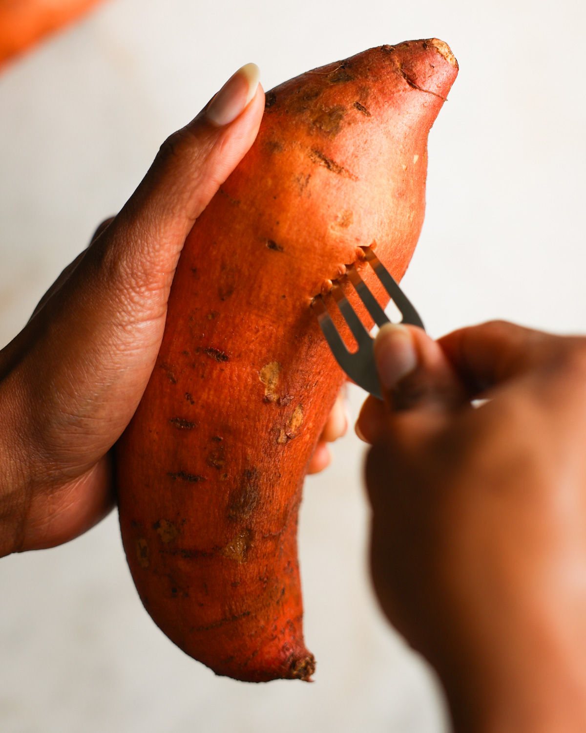 Brown hands piercing a sweet potato with a fork.