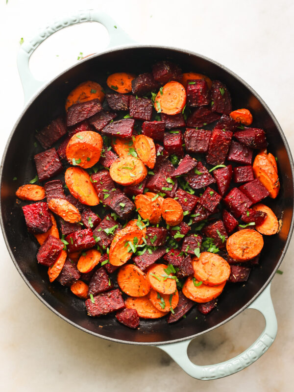 An overhead shot of a white pan of roasted beets and carrots with herbs.