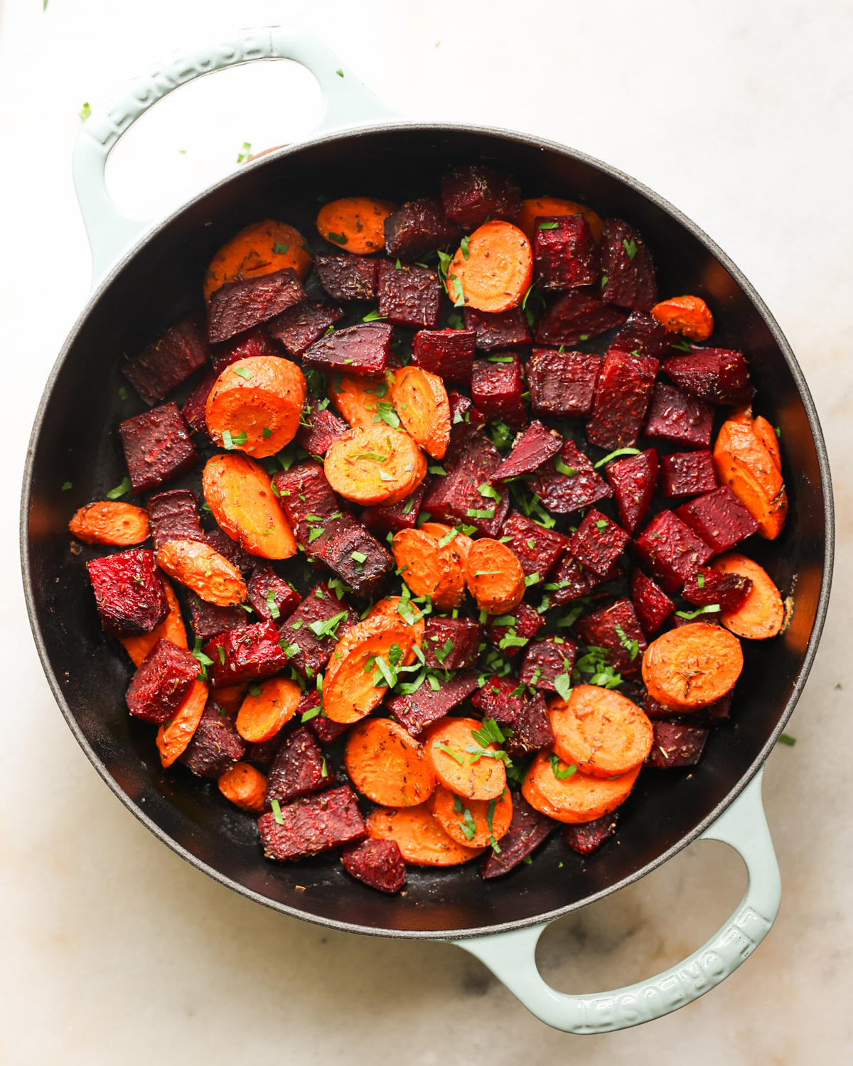 An overhead shot of a white pan of roasted beets and carrots with herbs.