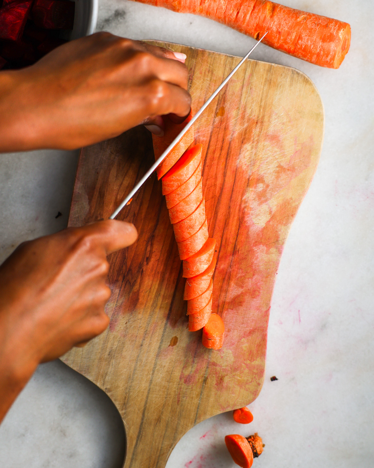 An overhead shot of brown hands slicing carrots on a diagonal.