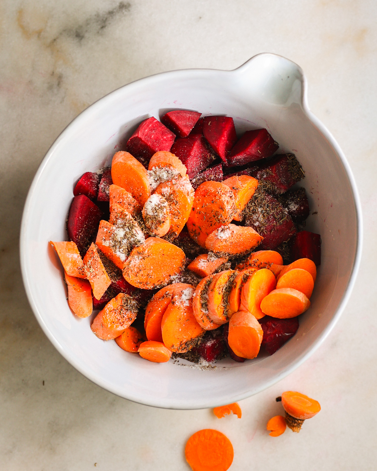 The beets and carrots in a mixing bowl with oil and seasoning before mixing.