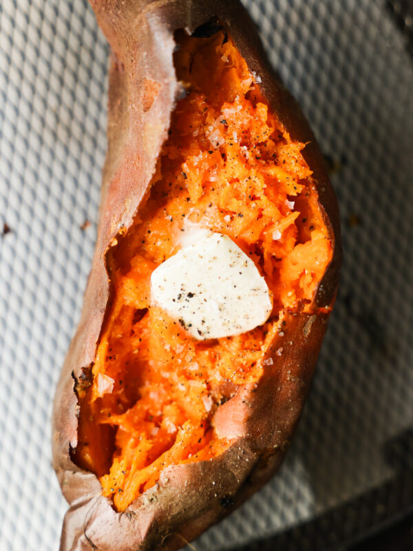 An overhead shot of an air fryer sweet potato, cut open and topped with butter, salt, and pepper.