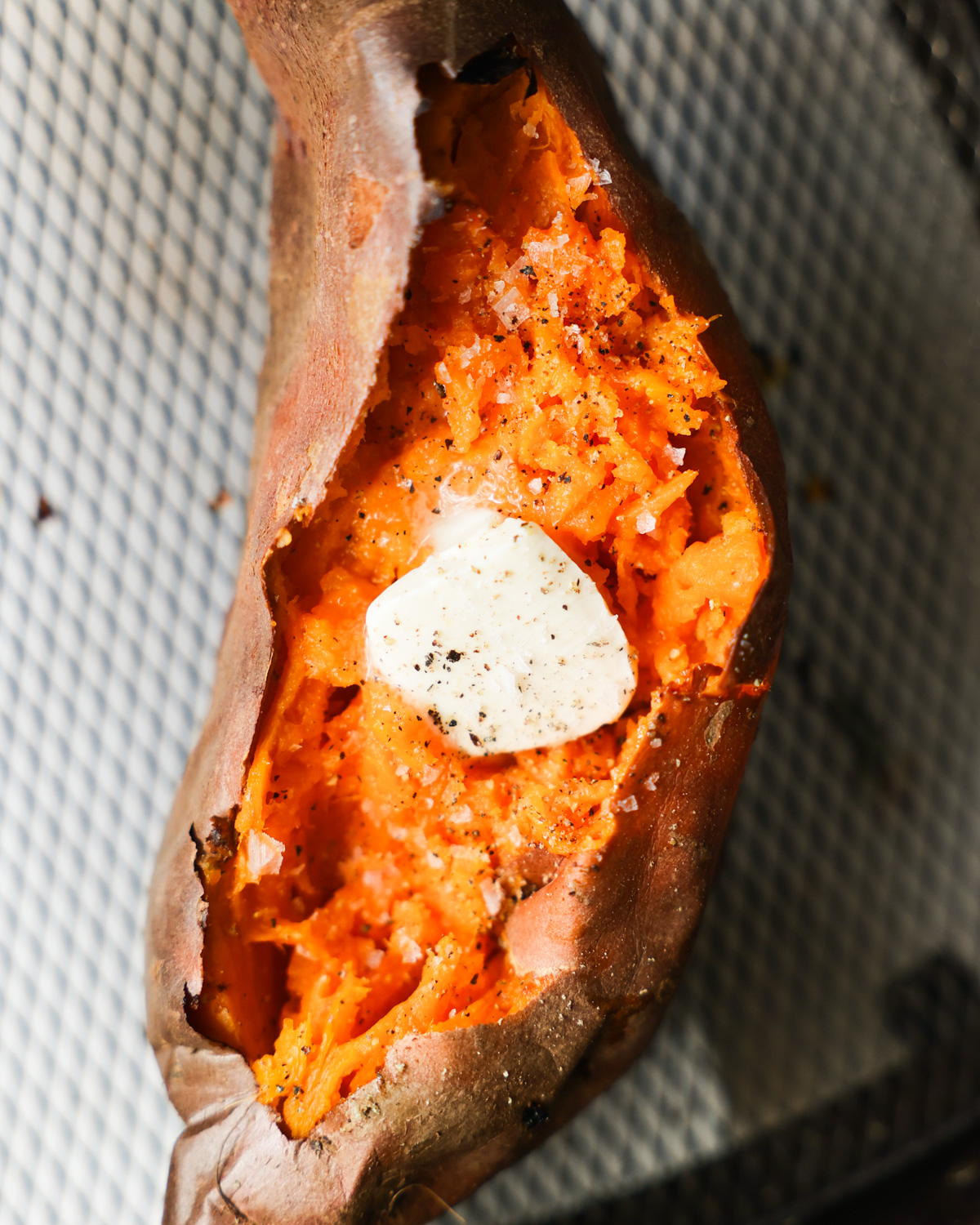 An overhead shot of an air fryer sweet potato, cut open and topped with butter, salt, and pepper.