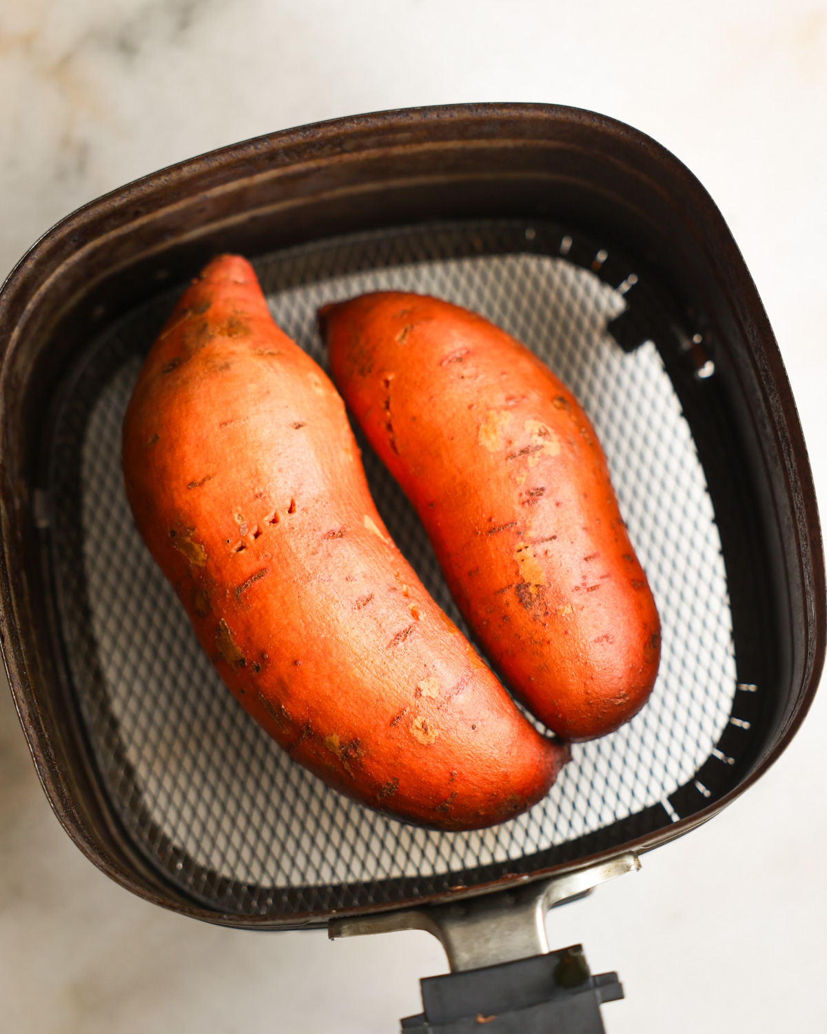 Two sweet potatoes pierced a few times with forks in the air fryer basket.