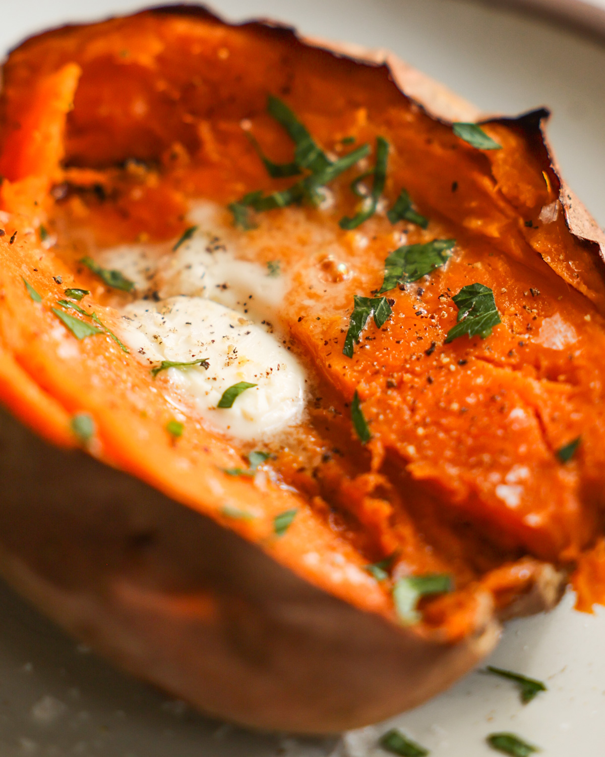 A close-up shot of an air fryer sweet potato cut open and topped with butter, salt and pepper, and chopped herbs.