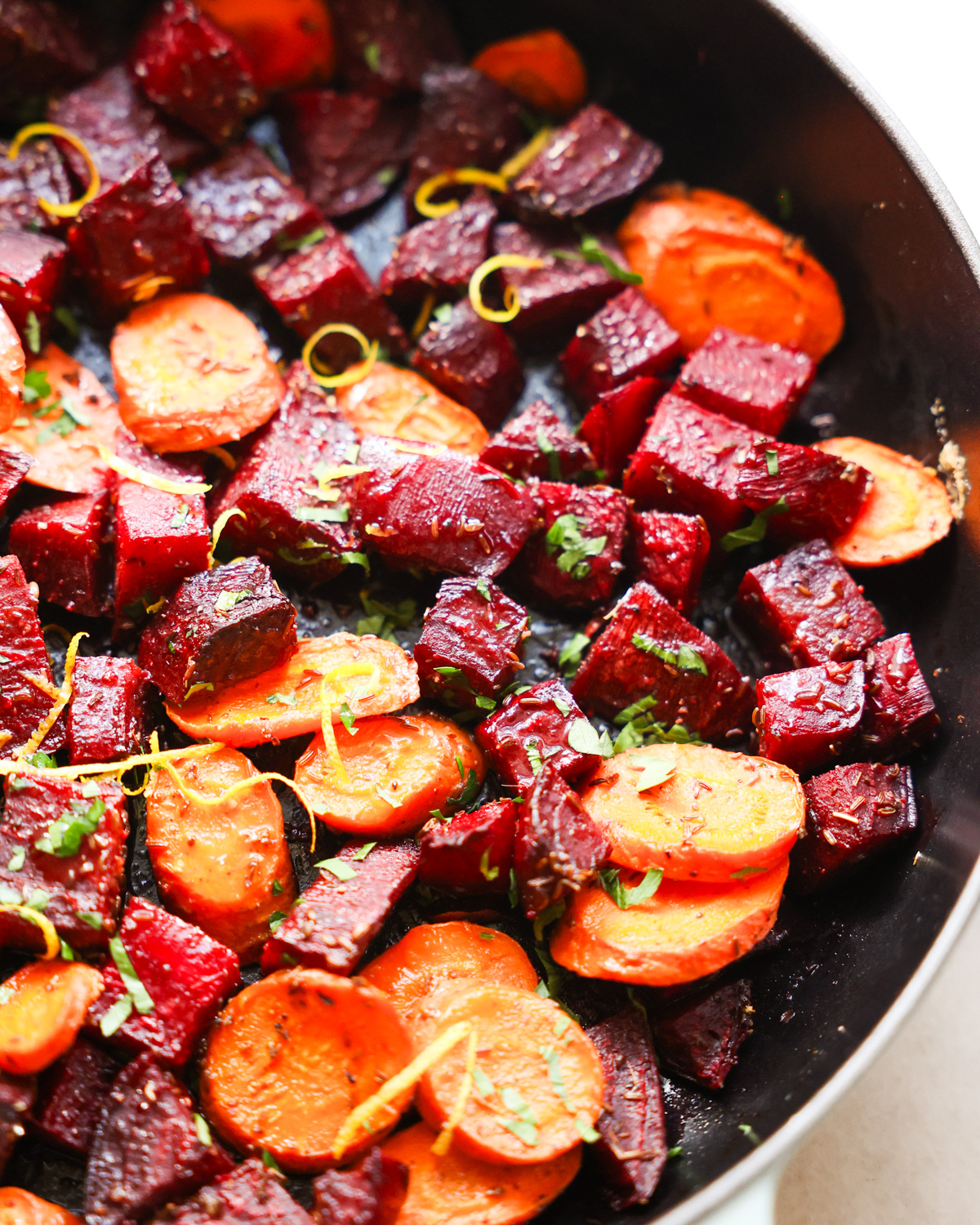 A close-up shot of a bowl of roasted beets and carrots with herbs.