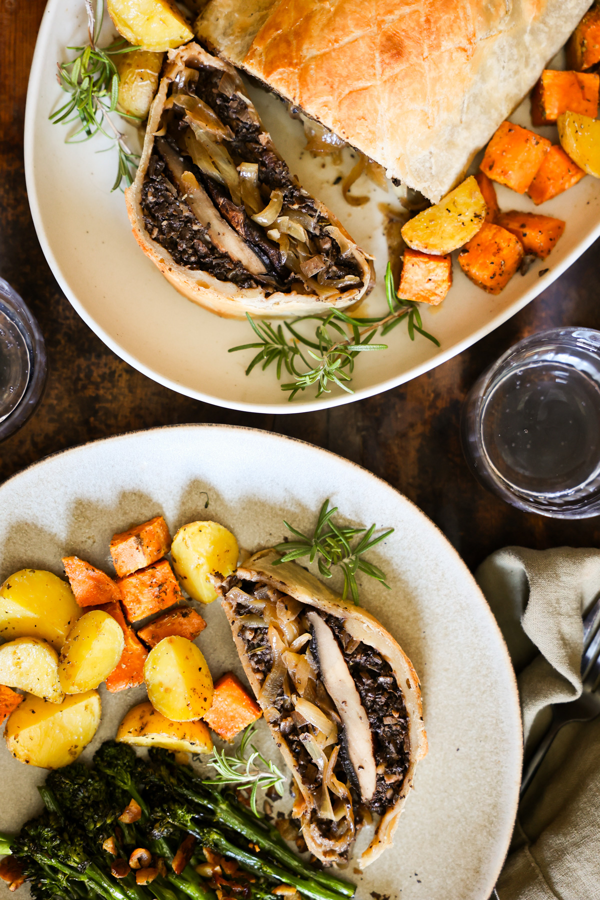 An overhead shot of a dinner plate with roasted vegetables and a piece of mushroom Wellington next to a serving plate of it.