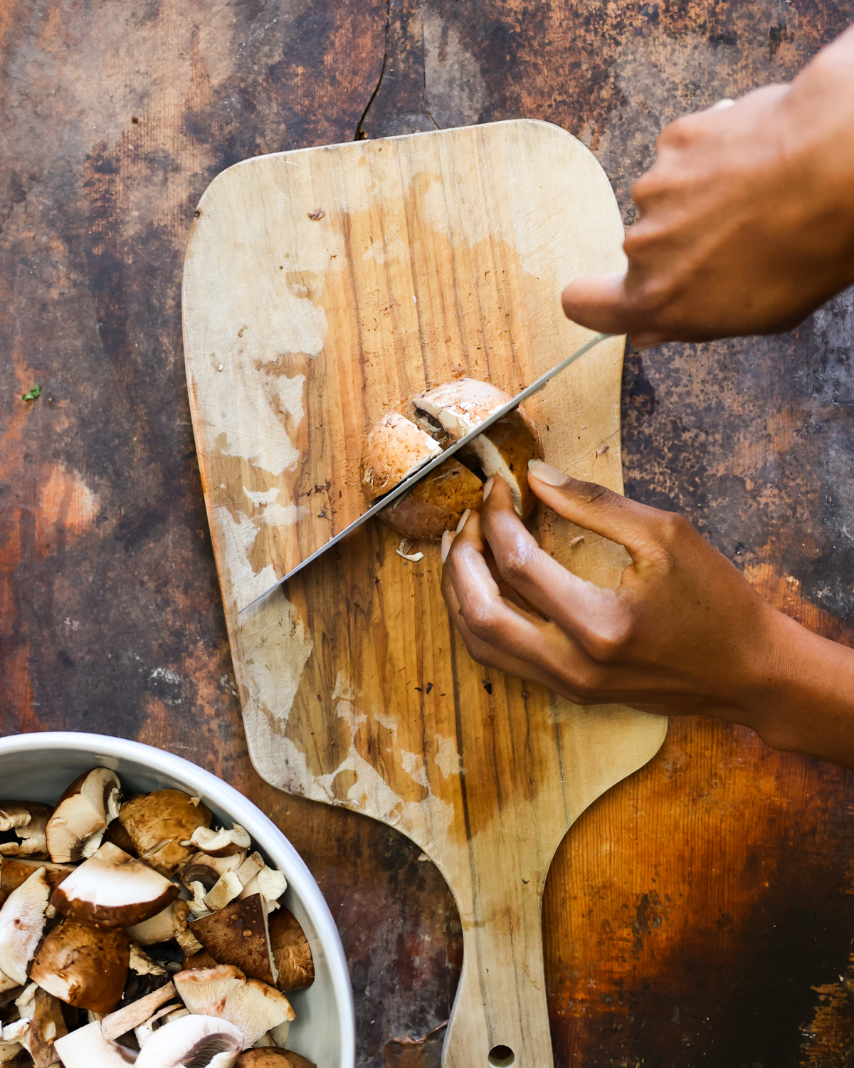 An overhead shot of two brown hands roughly chopping mushrooms.