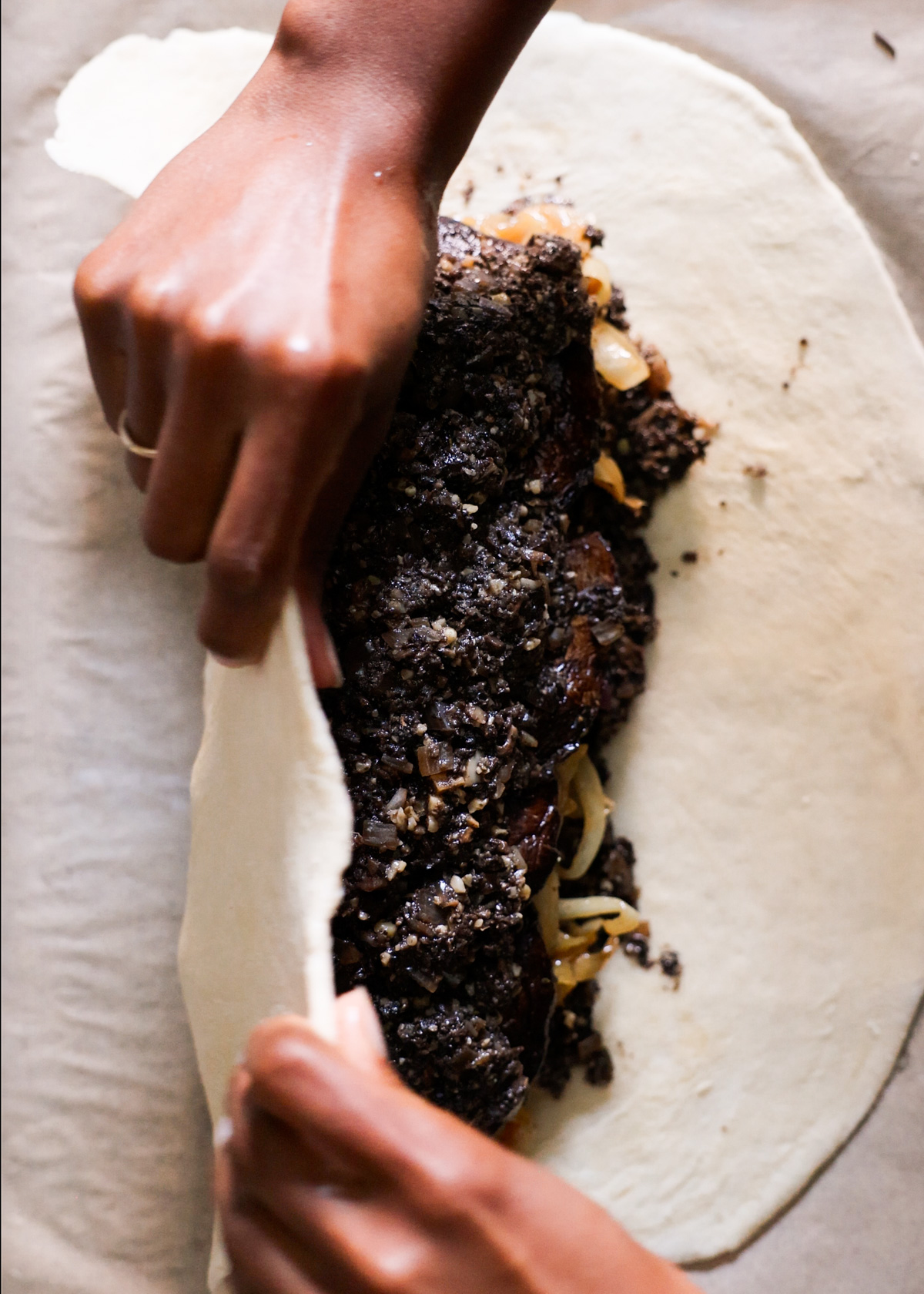 Two brown hands turning the pastry over the vegetable filling.