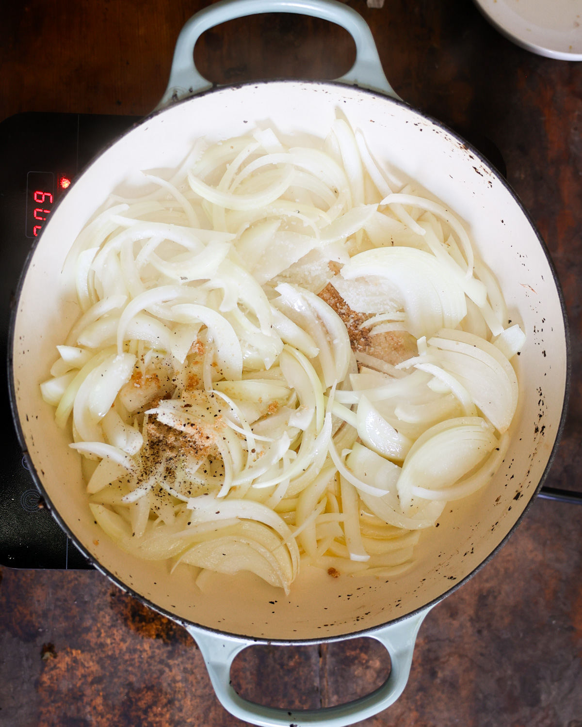 An overhead shot of the sliced onions with salt, pepper, and brown sugar in a pan.