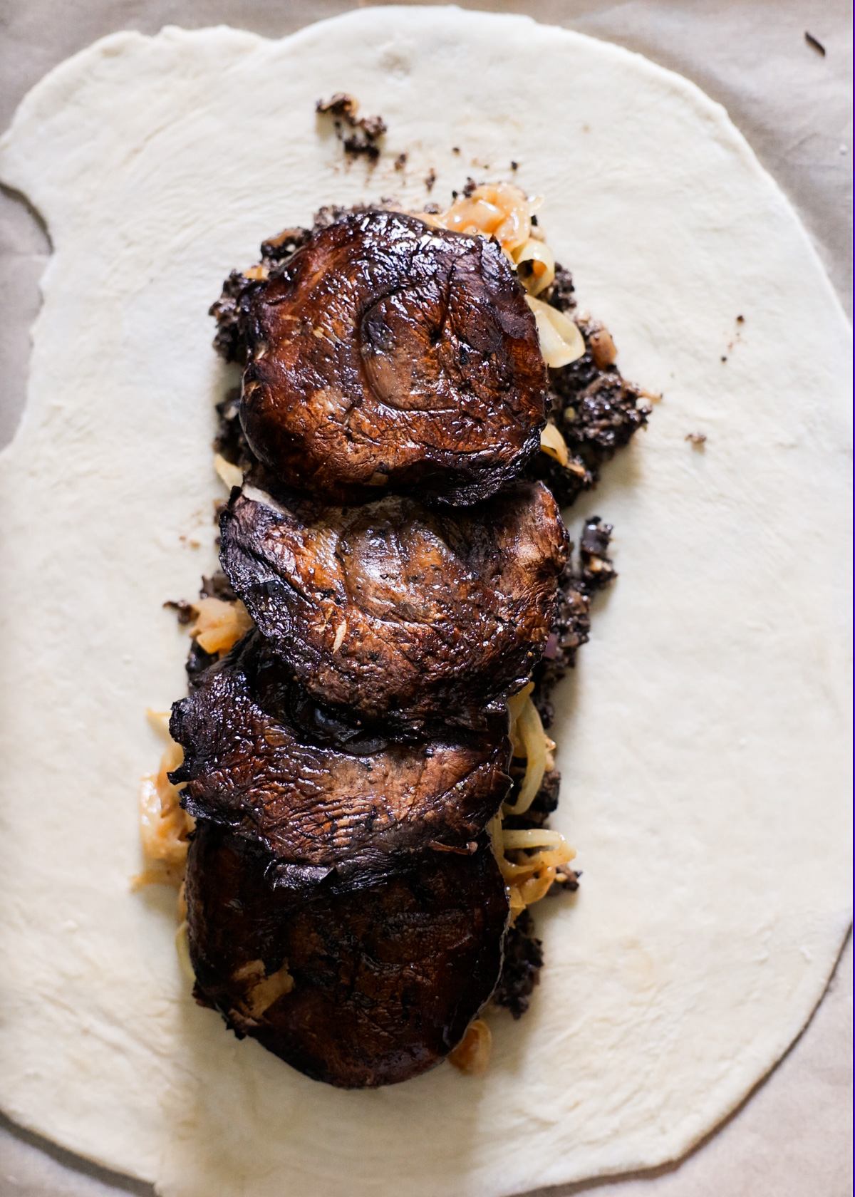 An overhead shot of puff pastry topped with the mushroom filling, caramelized onions, and portobello mushrooms layered on each other.