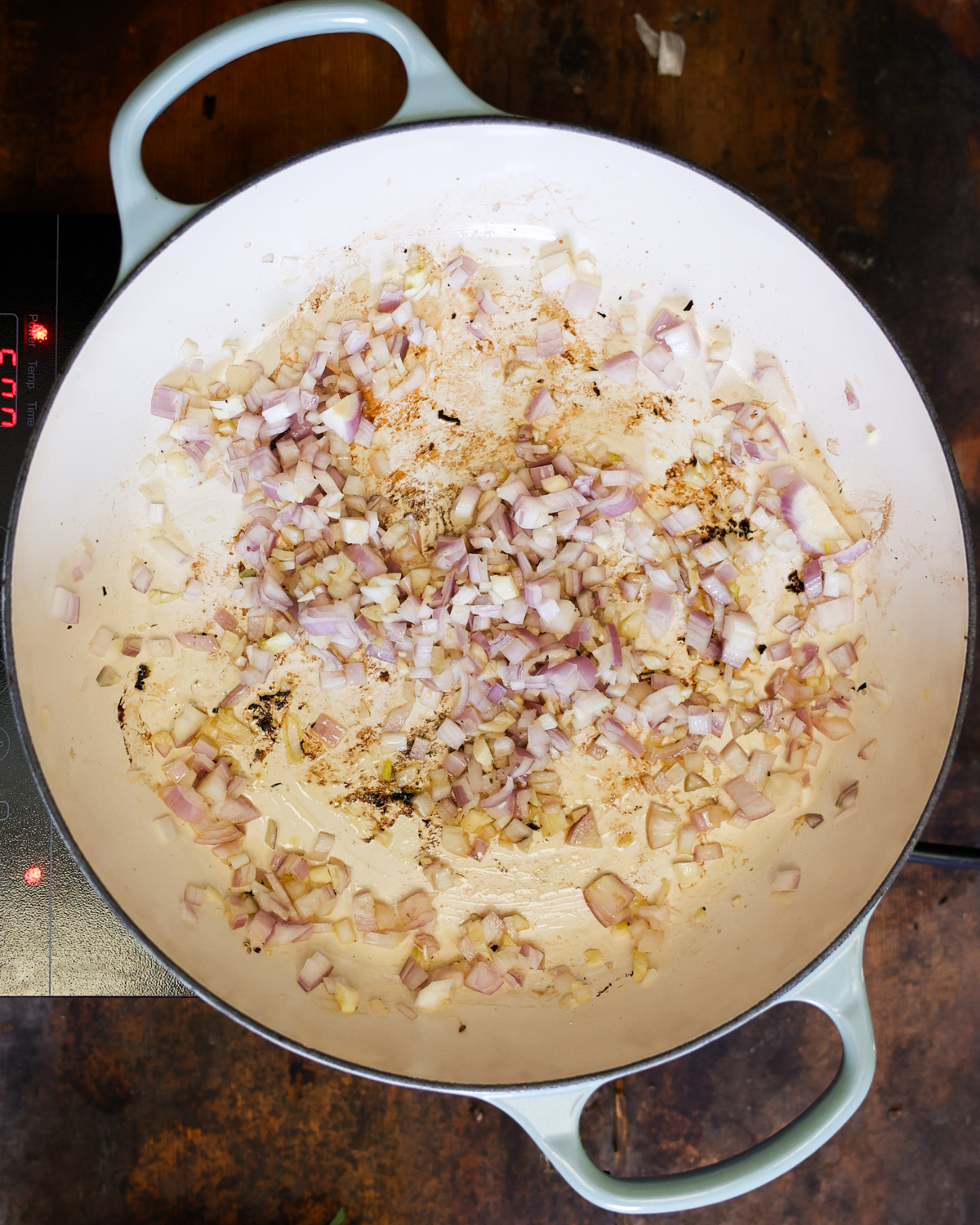 An overhead shot of shallots and onions cooking in a pan.