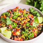 A close-up angled shot of a bowl of the black bean and corn salad with cilantro, jalapenos, and lime.