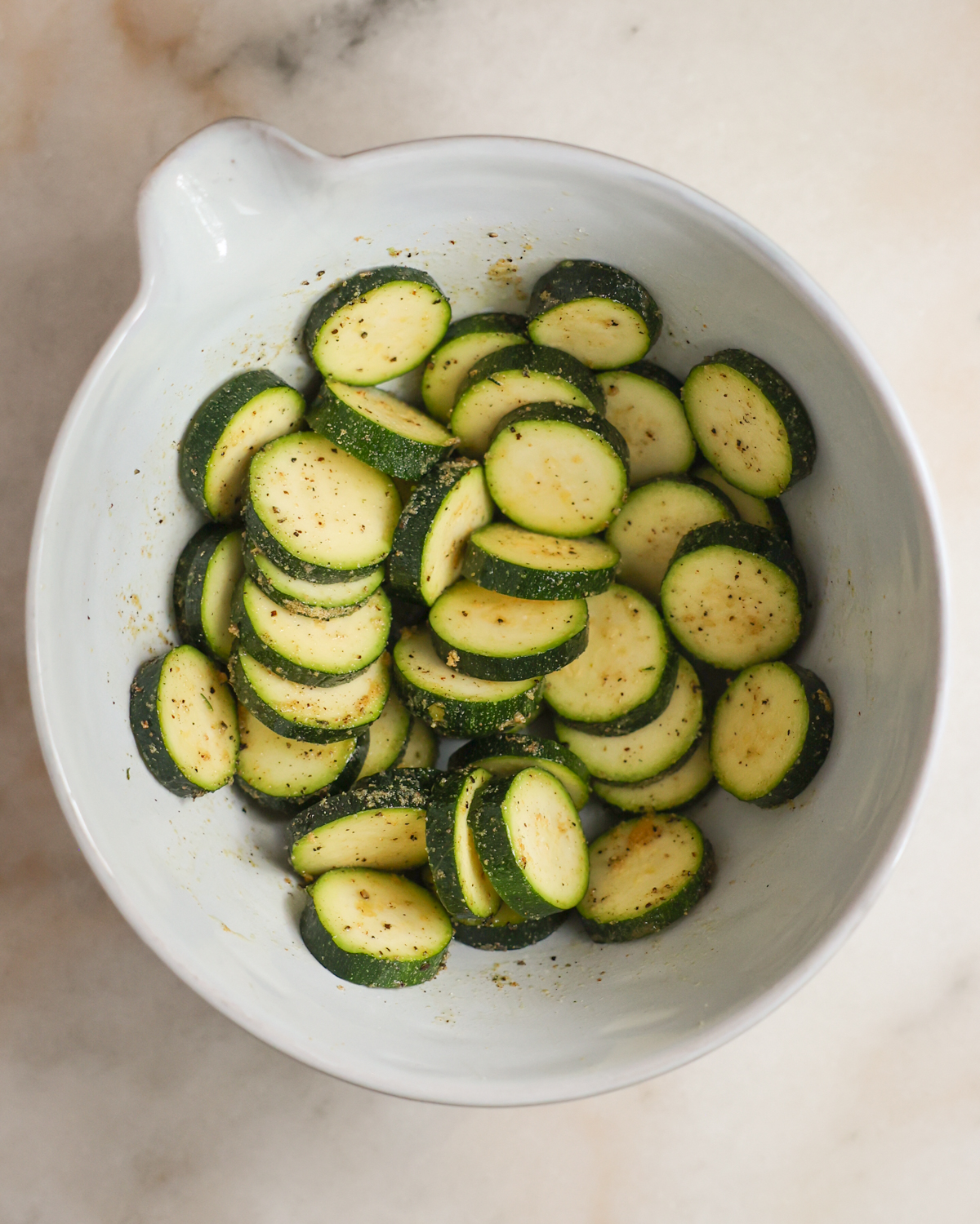 An overhead shot of a bowl of sliced, seasoned zucchini.