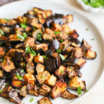 A close-up side shot of a serving plate of air fryer eggplant with chopped herbs.