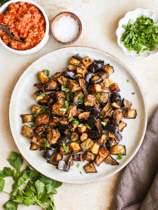 An overhead shot of a serving plate of air fryer eggplant next to small dishes of seasonings.