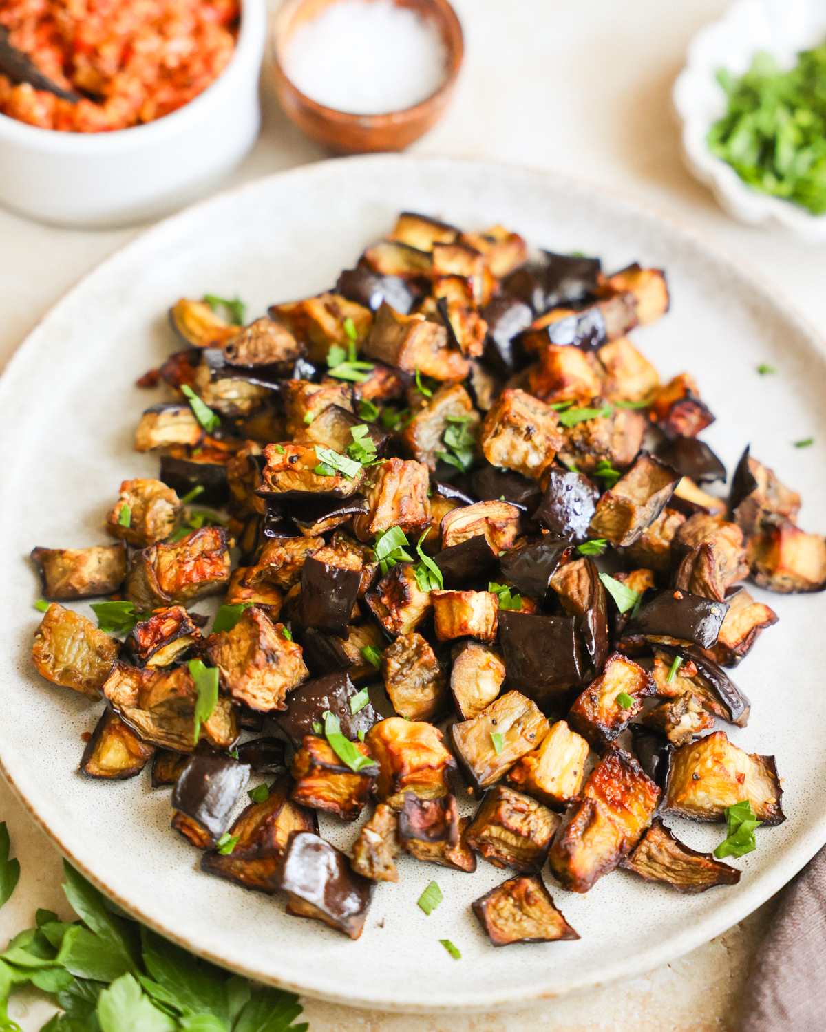 A close-up angled shot of a small serving plate of air fryer eggplant topped with chopped herbs.