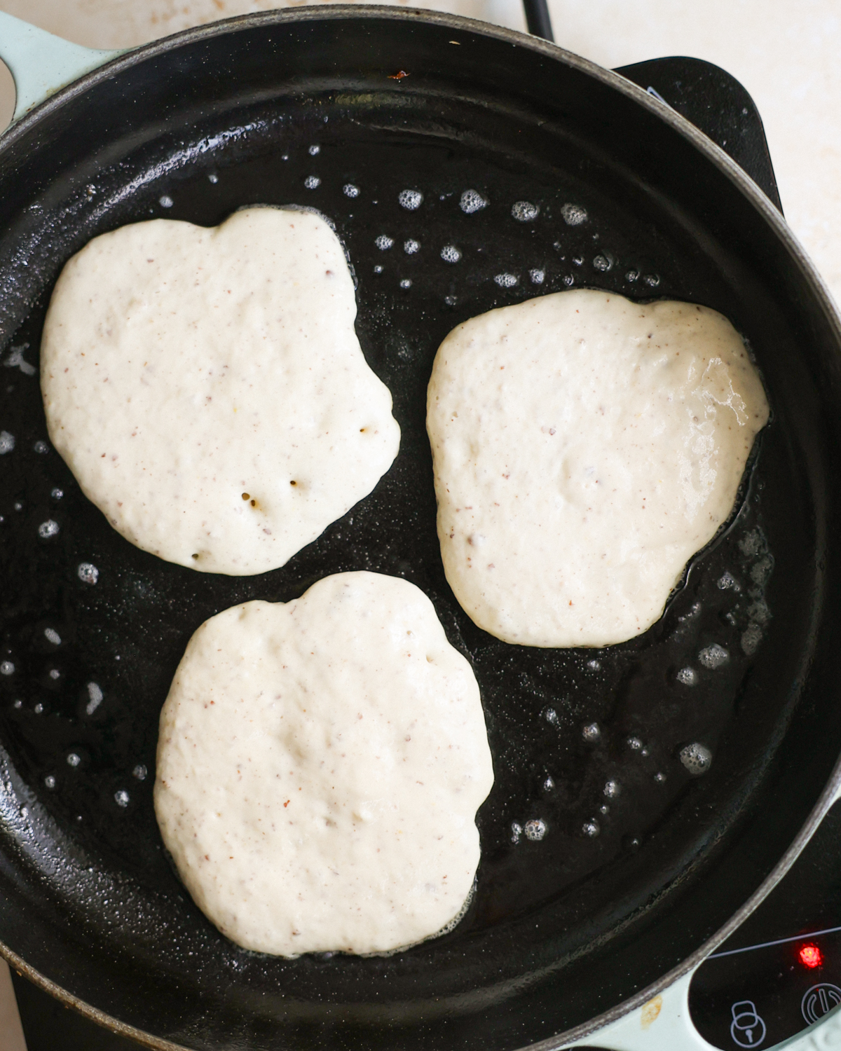 Three sourdough discard pancakes cooking on a griddle.