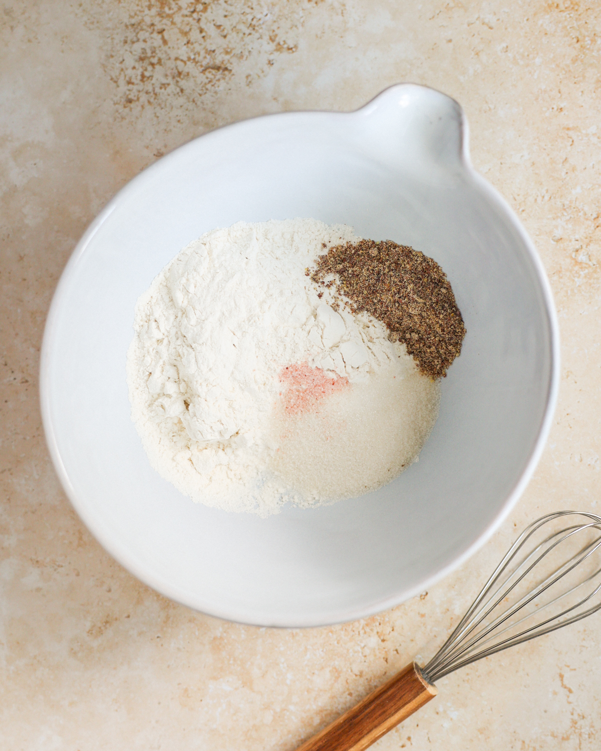 An overhead shot of the dry ingredients added to a large mixing bowl next to a whisk.