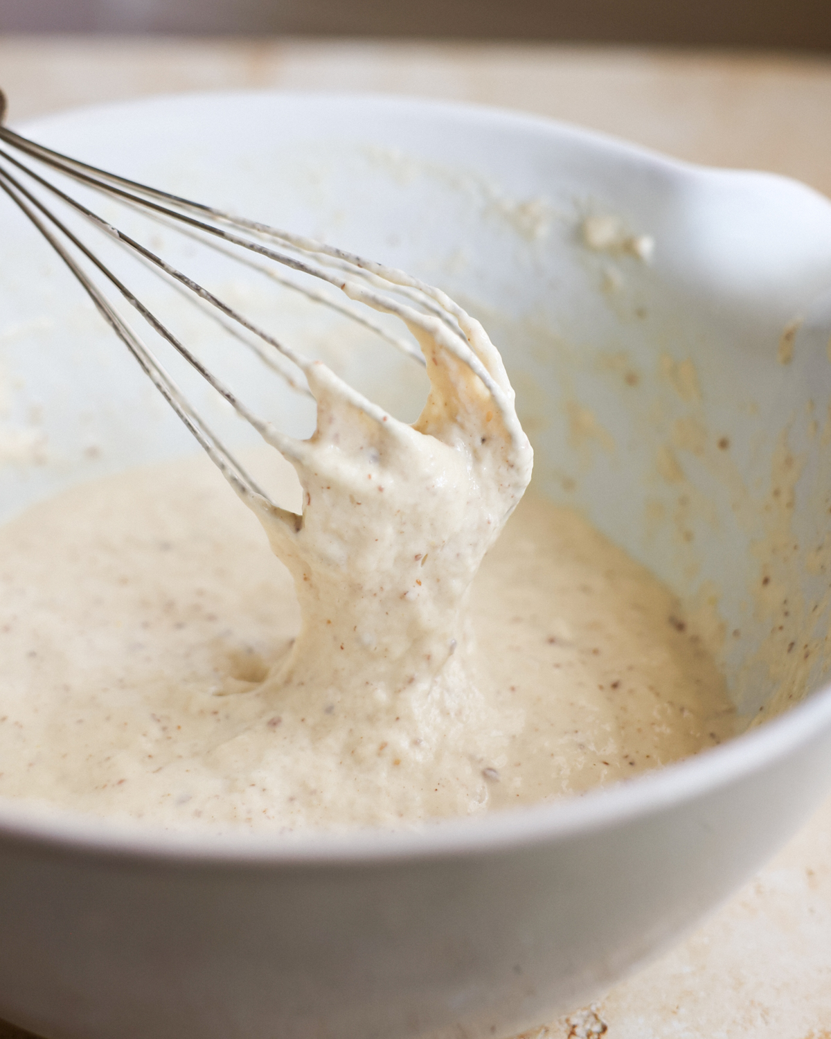 A close-up shot of the sourdough discard pancake batter dripping from a whisk into a mixing bowl.
