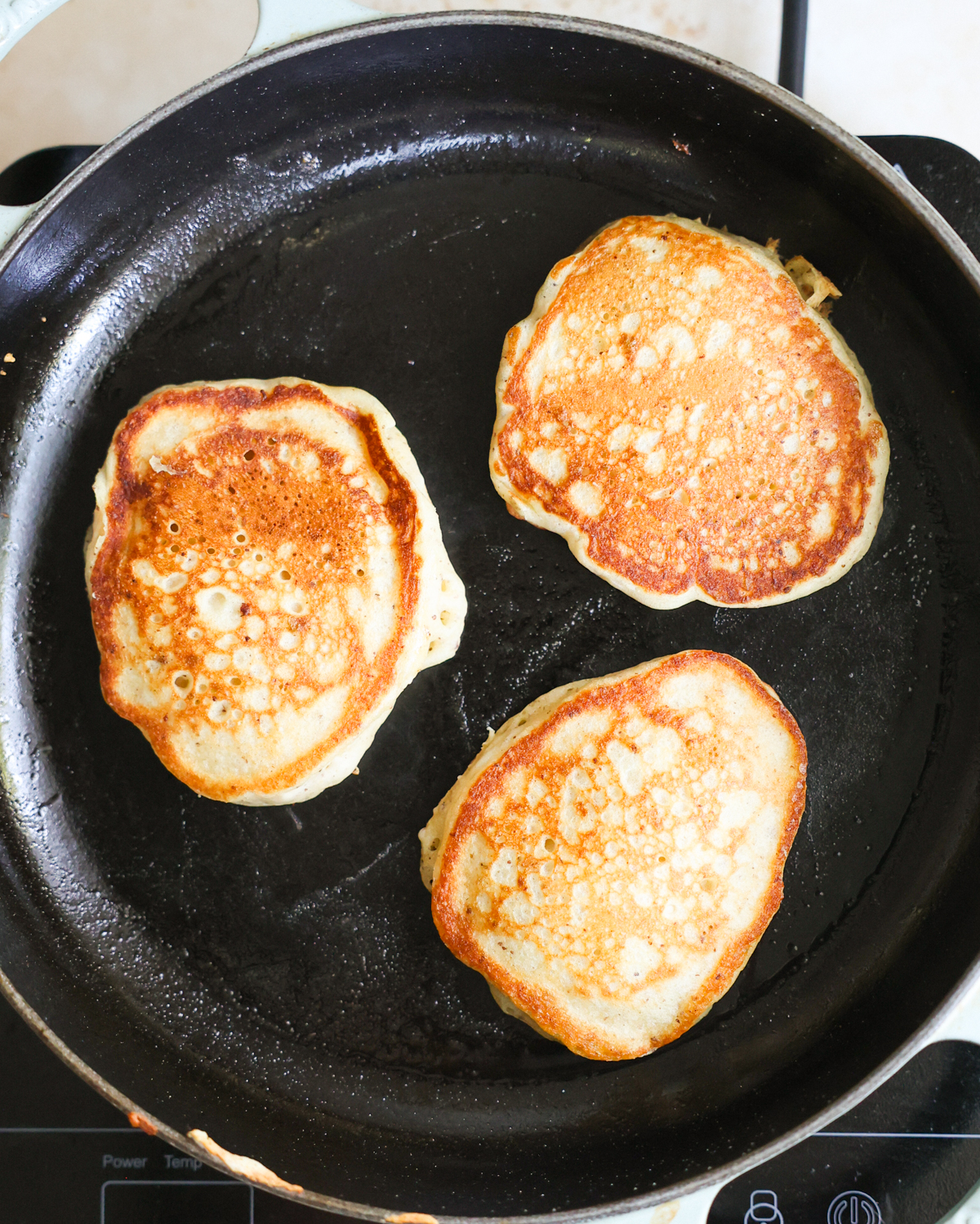 An overhead shot of three sourdough discard pancakes cooking on the griddle.