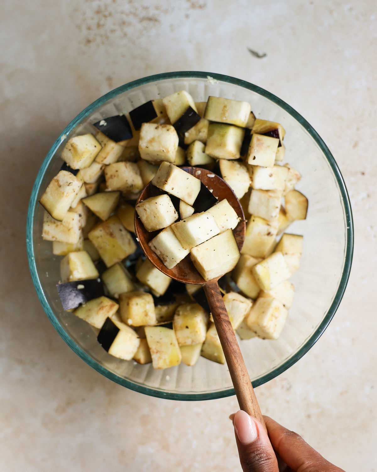 A brown hand holding a stirring spoon with seasoned eggplant on it.