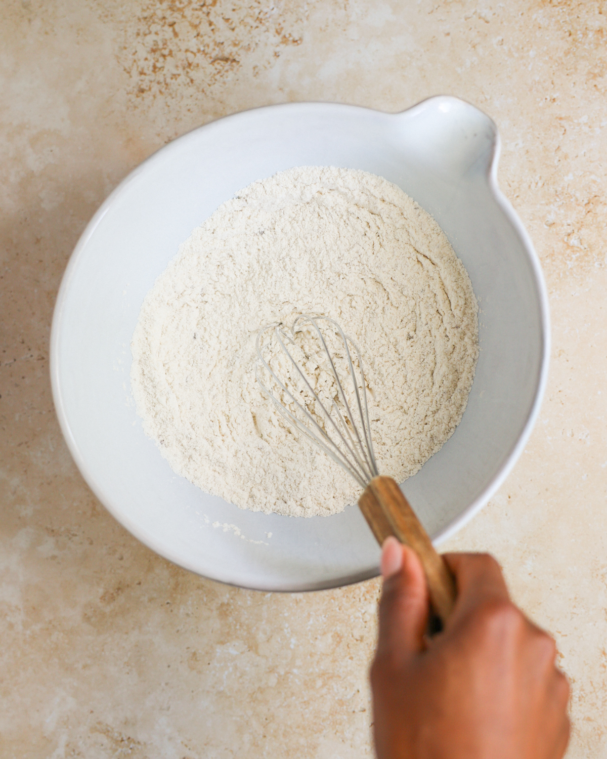 A brown hand whisking the bowl of dry ingredients.