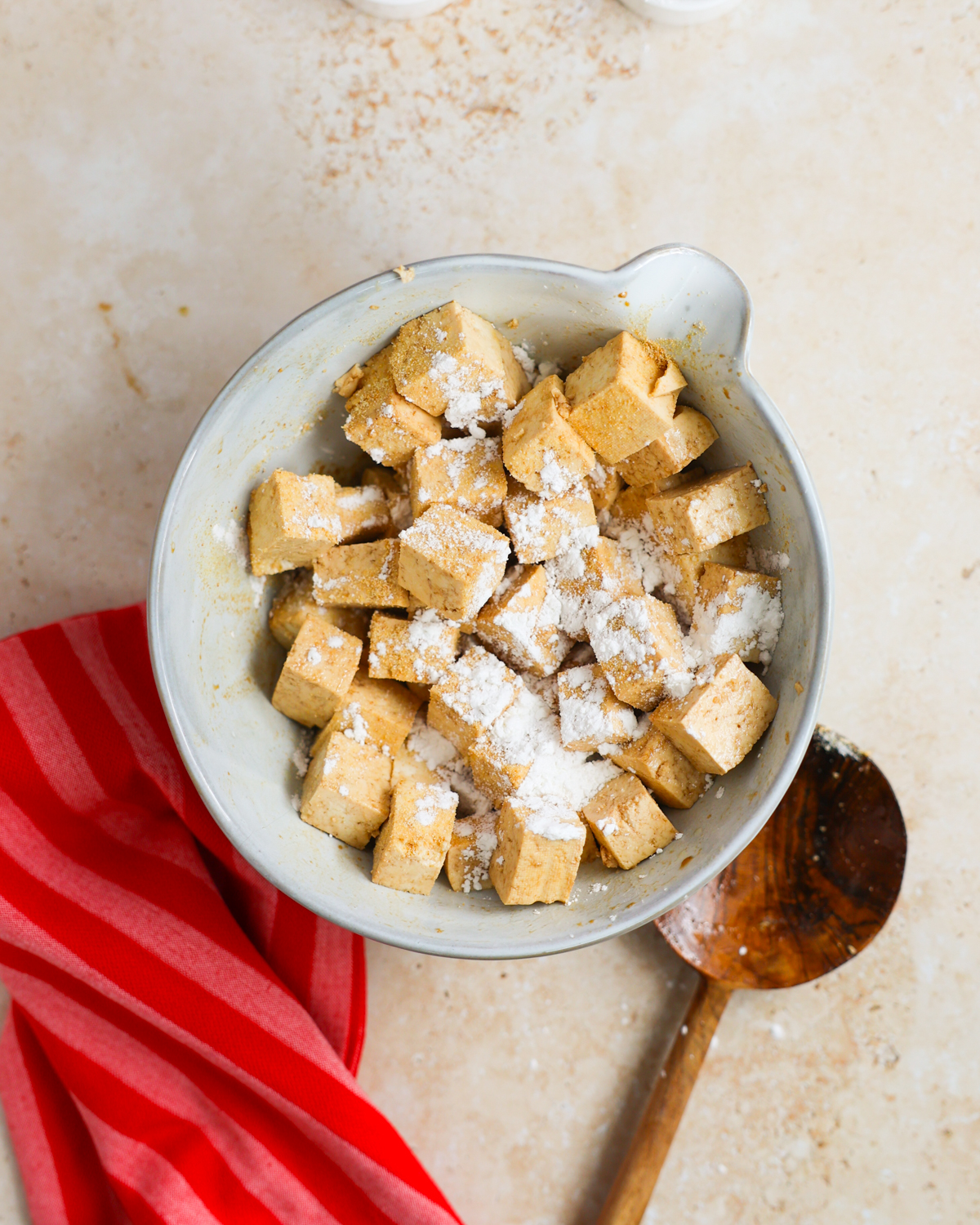 overhead of tofu topped with cornstarch in mixing bowl