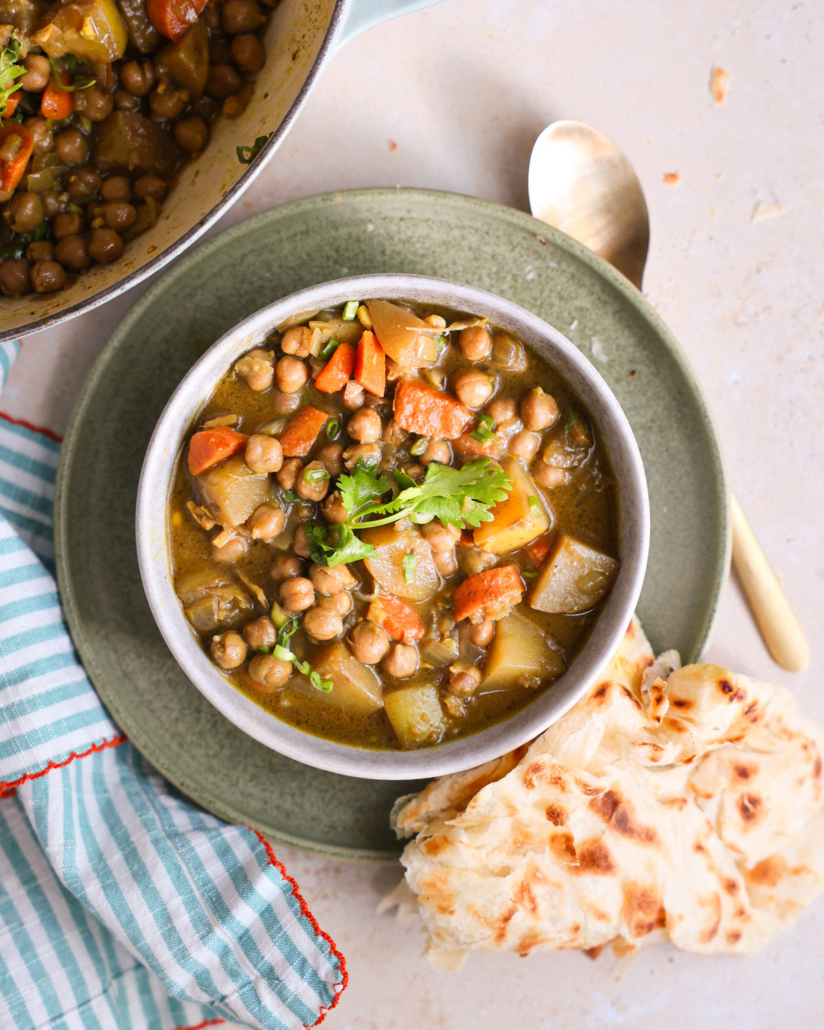 An overhead shot of a bowl of Jamaican chickpea curry on the counter next to the pot and pieces of roti.