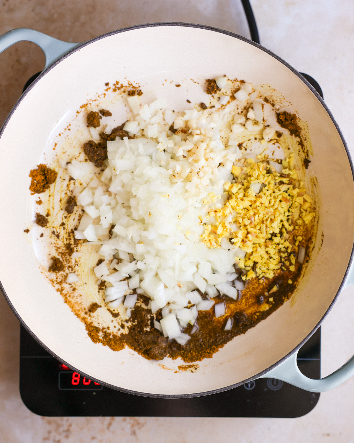 A white pan of toasted curry paste with onions, garlic, and ginger added.