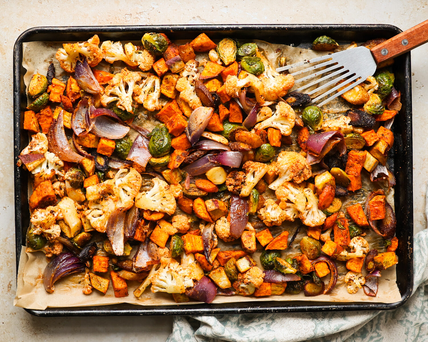 Stirring roasted vegetables on a baking tray.